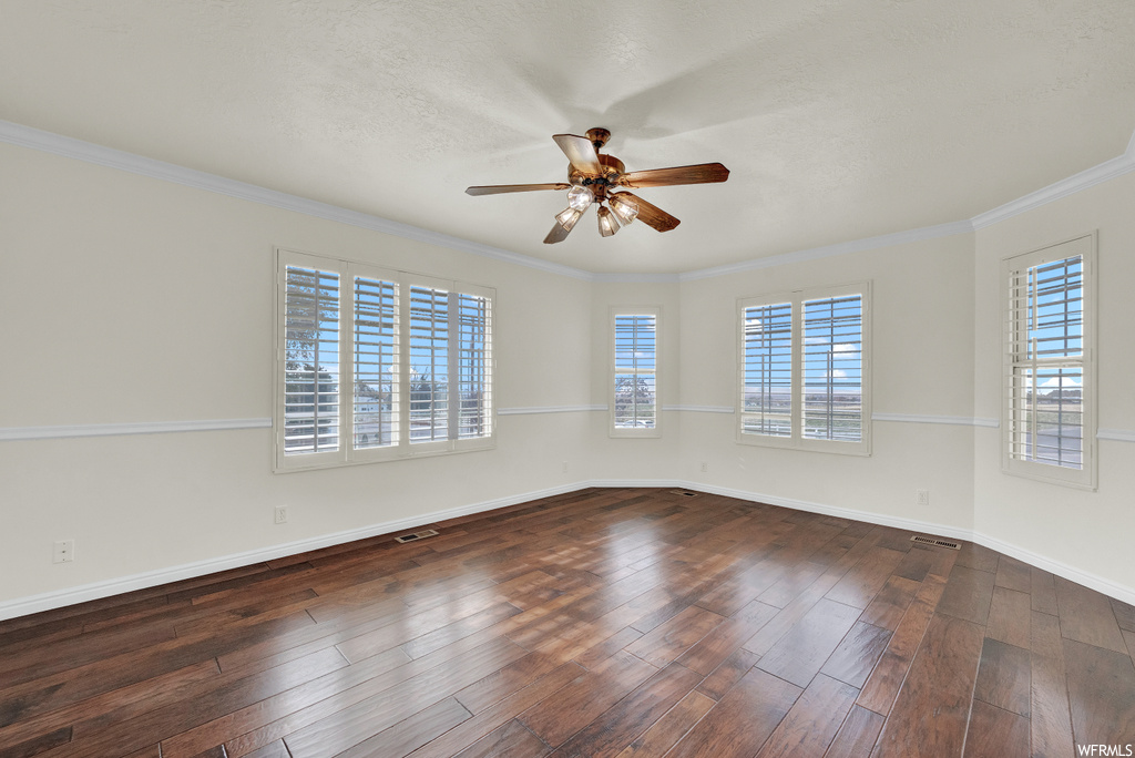Empty room featuring dark wood-type flooring, ceiling fan, and crown molding