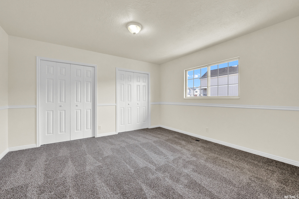 Unfurnished bedroom featuring multiple closets and dark colored carpet