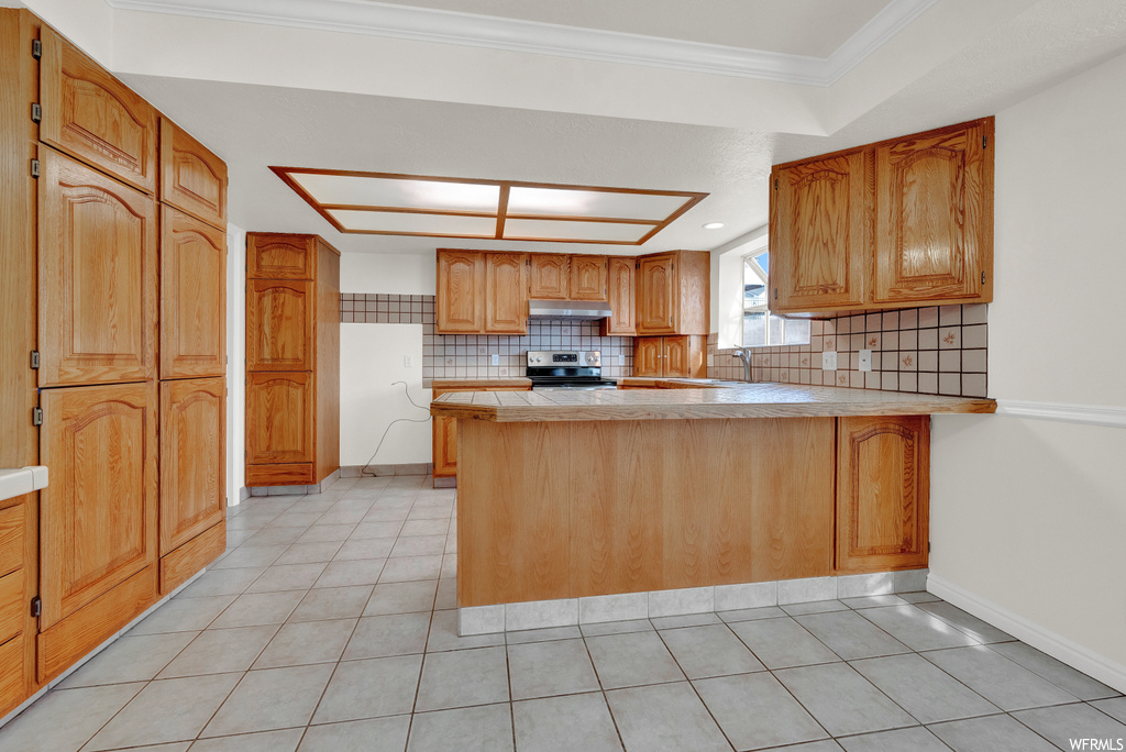 Kitchen featuring light tile floors, crown molding, electric stove, kitchen peninsula, and tasteful backsplash