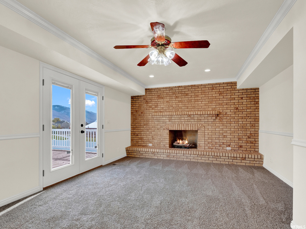 Unfurnished living room with ceiling fan, ornamental molding, carpet floors, a brick fireplace, and brick wall
