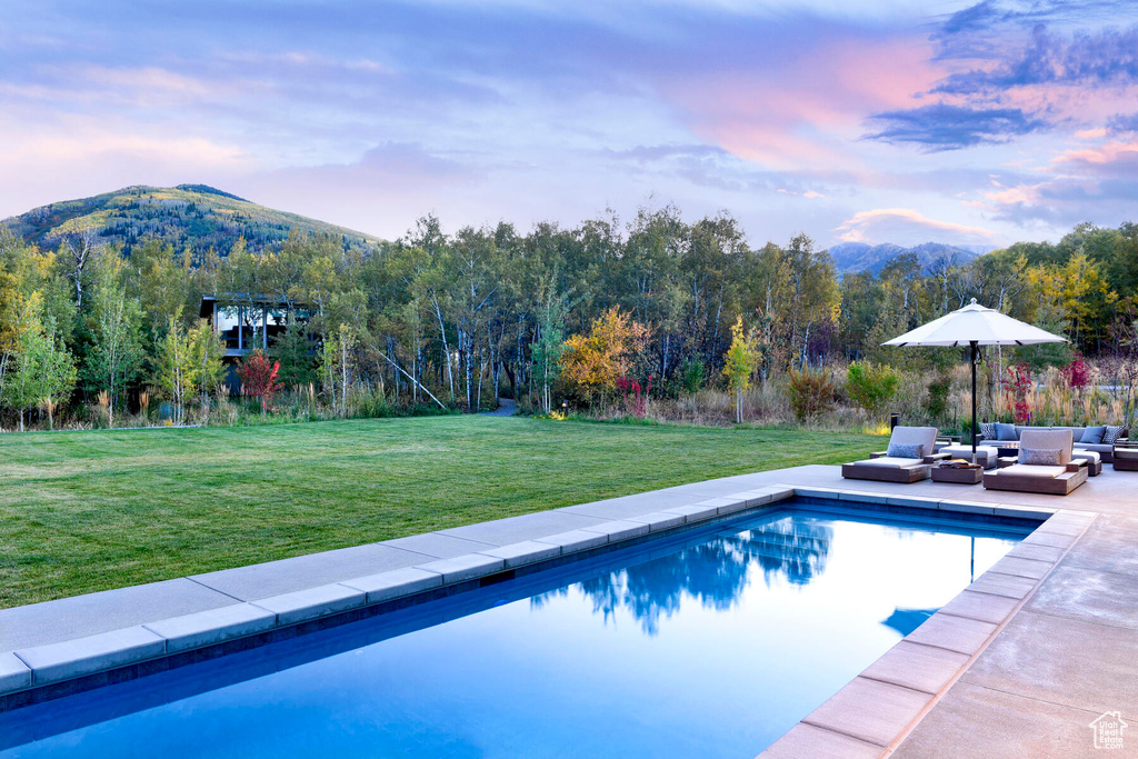Pool at dusk with a mountain view, an outdoor living space, a lawn, and a patio area