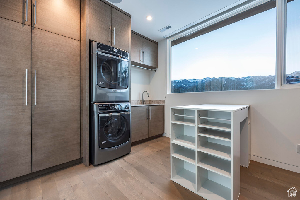 Clothes washing area featuring a mountain view, sink, stacked washer / drying machine, light hardwood / wood-style floors, and cabinets