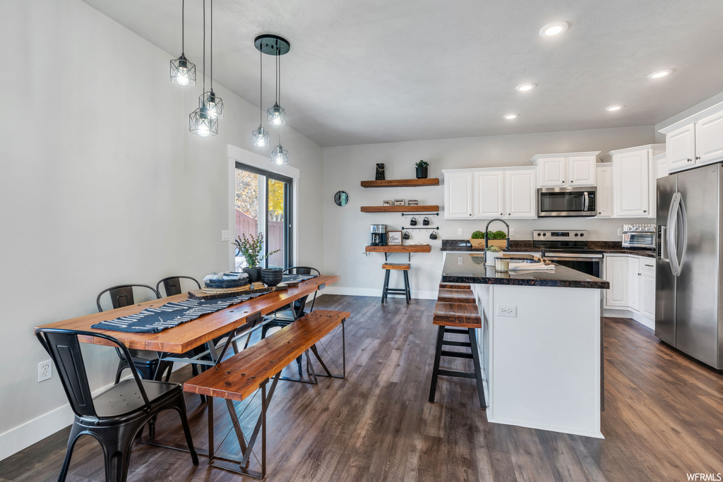 Kitchen with a kitchen breakfast bar, appliances with stainless steel finishes, pendant lighting, dark hardwood / wood-style floors, and white cabinetry