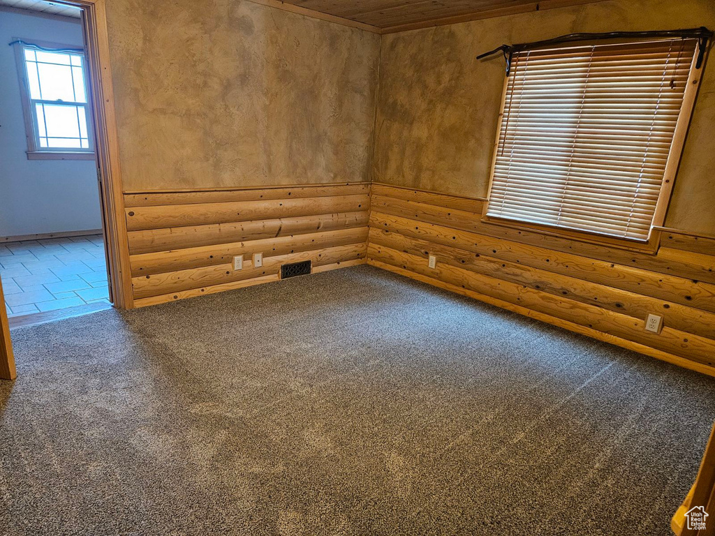 Empty room featuring wood ceiling, carpet flooring, and rustic walls