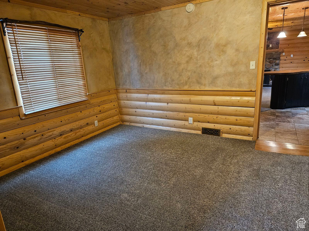 Carpeted spare room featuring log walls and wood ceiling