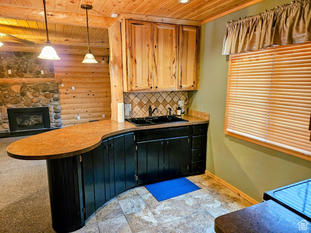 Kitchen featuring backsplash, wooden ceiling, sink, pendant lighting, and a stone fireplace