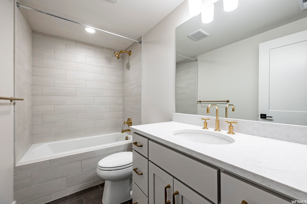 Full bathroom featuring tiled shower / bath combo, toilet, tile floors, and oversized vanity