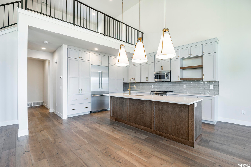 Kitchen with sink, a center island with sink, hanging light fixtures, stainless steel appliances, and dark hardwood / wood-style floors