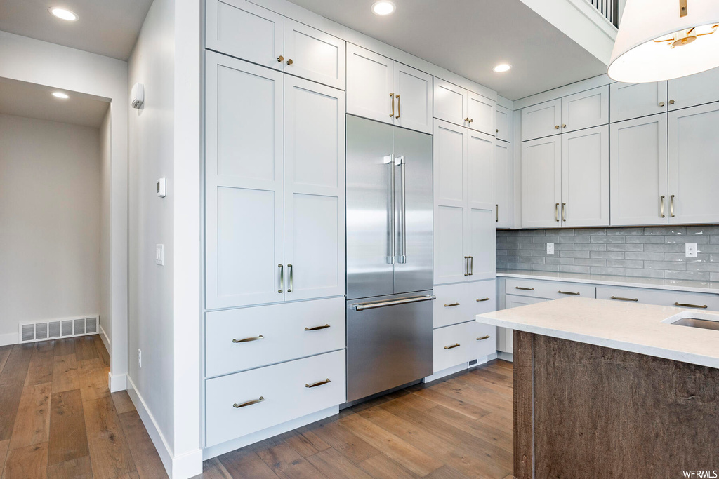 Kitchen featuring white cabinets, hardwood / wood-style flooring, backsplash, and stainless steel built in refrigerator
