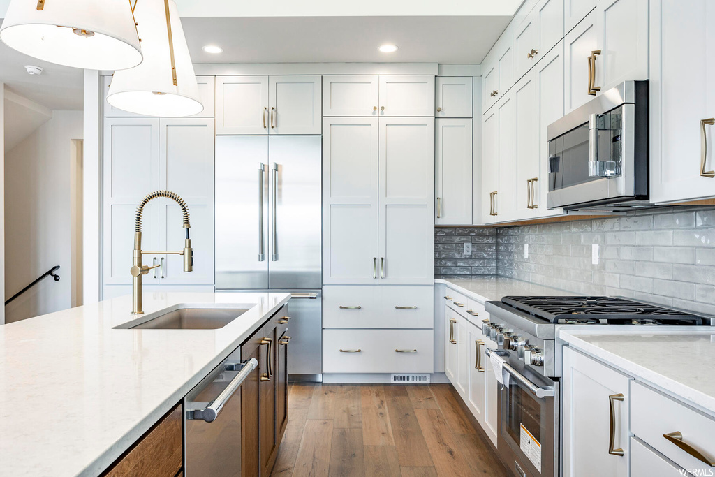 Kitchen featuring white cabinets, sink, high end appliances, and hardwood / wood-style floors