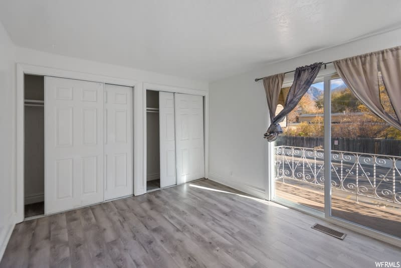 Unfurnished bedroom with access to outside, multiple closets, and hardwood / wood-style flooring