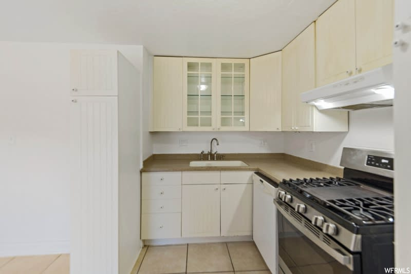Kitchen featuring sink, white dishwasher, cream cabinetry, light tile floors, and gas range