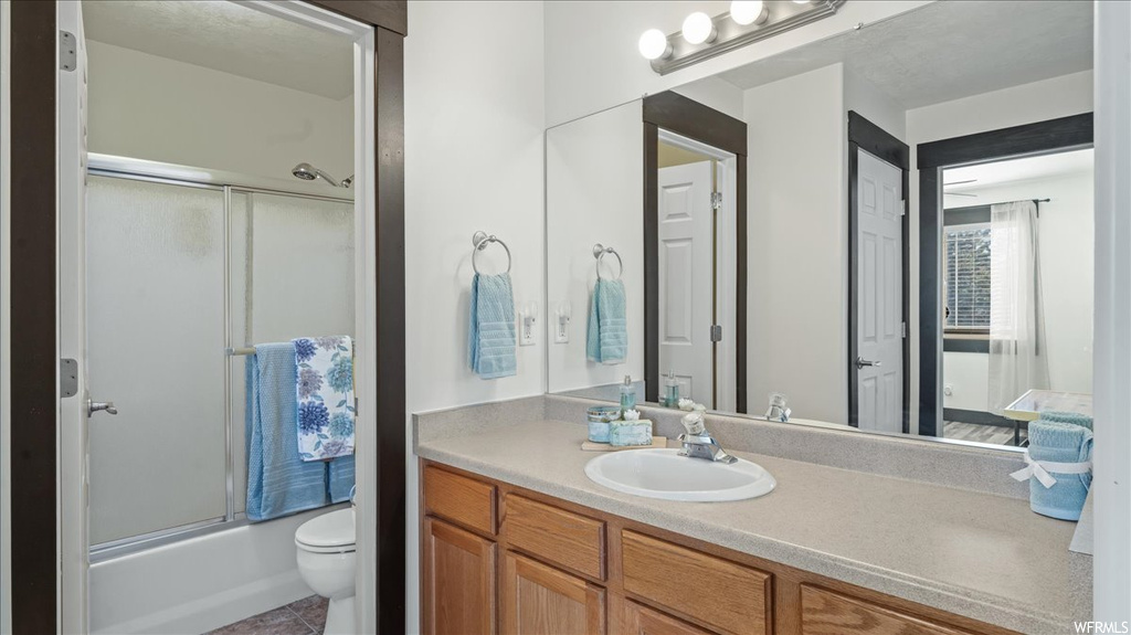 Full bathroom featuring toilet, tile flooring, oversized vanity, and shower / bath combination with glass door