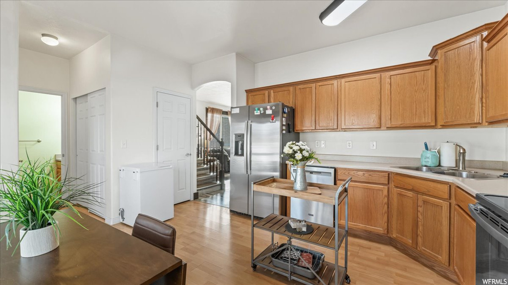 Kitchen featuring sink, stainless steel fridge, light hardwood / wood-style floors, and range with electric cooktop