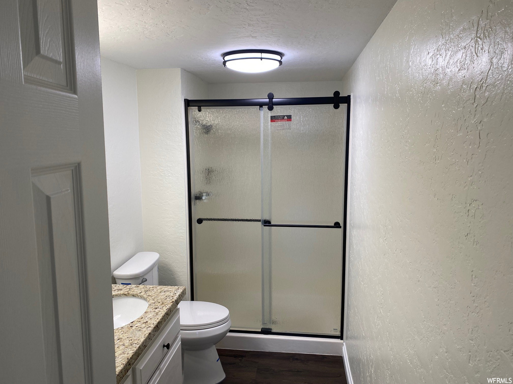 Bathroom featuring vanity, hardwood / wood-style flooring, an enclosed shower, toilet, and a textured ceiling