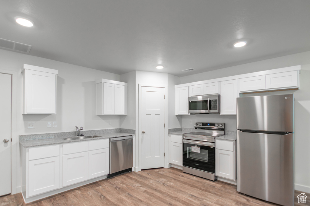 Kitchen with stainless steel appliances, light wood-type flooring, and white cabinetry