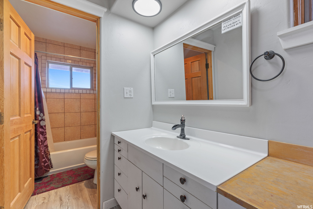 Full bathroom with toilet, shower / bath combo with shower curtain, wood-type flooring, and vanity with extensive cabinet space