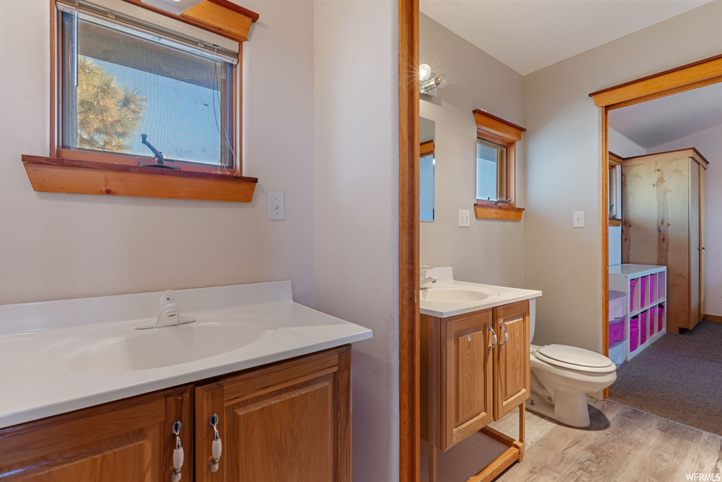 Bathroom with a healthy amount of sunlight, toilet, vanity with extensive cabinet space, and hardwood / wood-style flooring