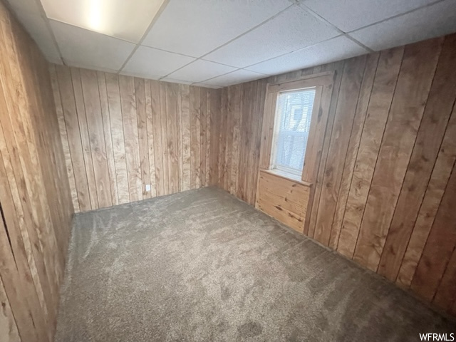 Carpeted spare room featuring a paneled ceiling and wood walls