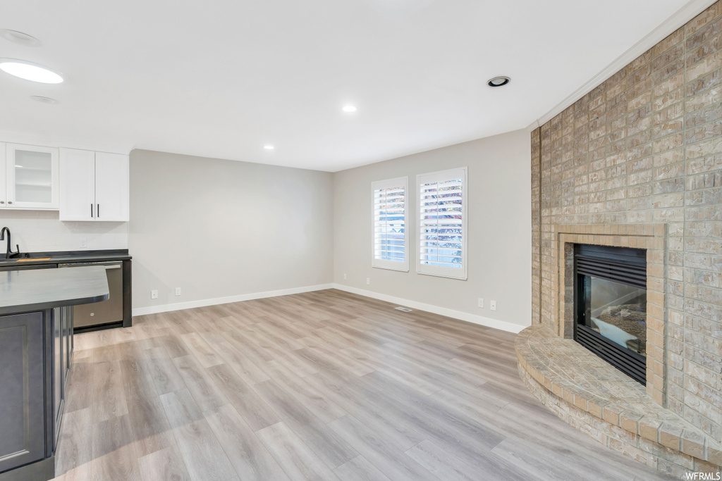 Unfurnished living room with a brick fireplace, light wood-type flooring, brick wall, and sink