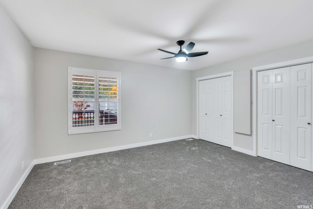 Unfurnished bedroom with dark carpet, multiple closets, and ceiling fan