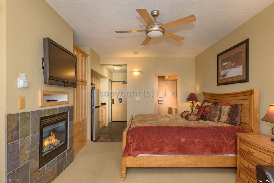 Bedroom featuring ceiling fan, a textured ceiling, stainless steel fridge, a tile fireplace, and light carpet