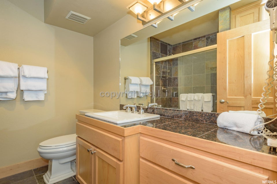 Bathroom with toilet, tile flooring, an enclosed shower, and vanity with extensive cabinet space
