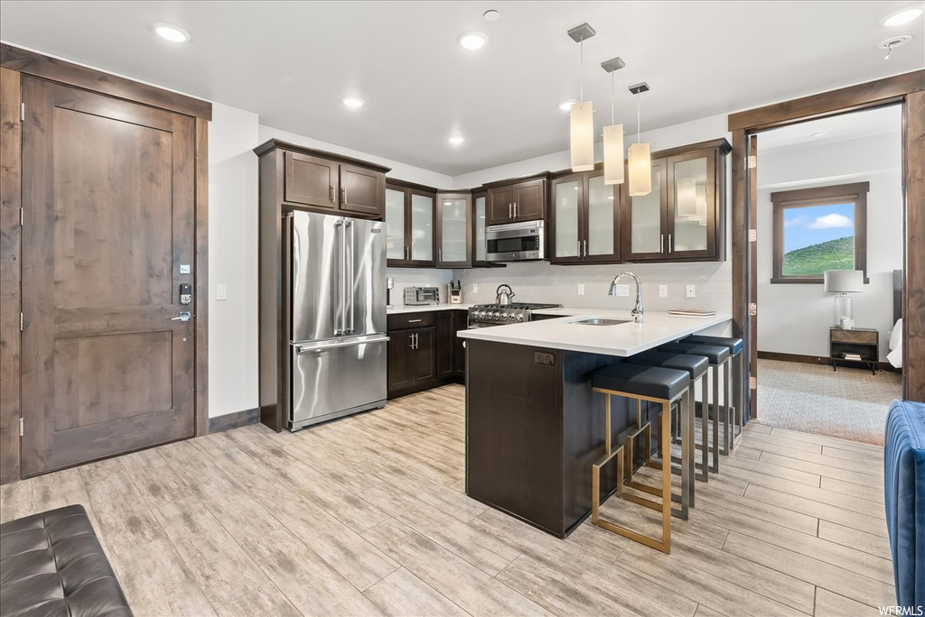 Kitchen featuring dark brown cabinetry, stainless steel appliances, tasteful backsplash, decorative light fixtures, and a kitchen breakfast bar