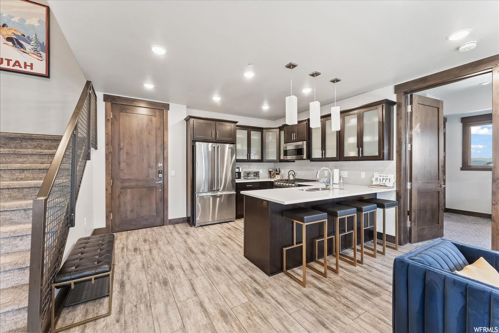 Kitchen featuring light wood-type flooring, dark brown cabinetry, pendant lighting, and stainless steel appliances