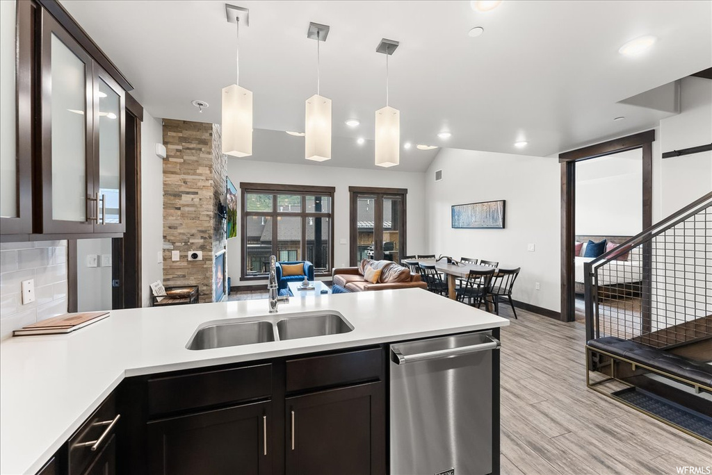 Kitchen with hanging light fixtures, sink, stainless steel dishwasher, backsplash, and light wood-type flooring