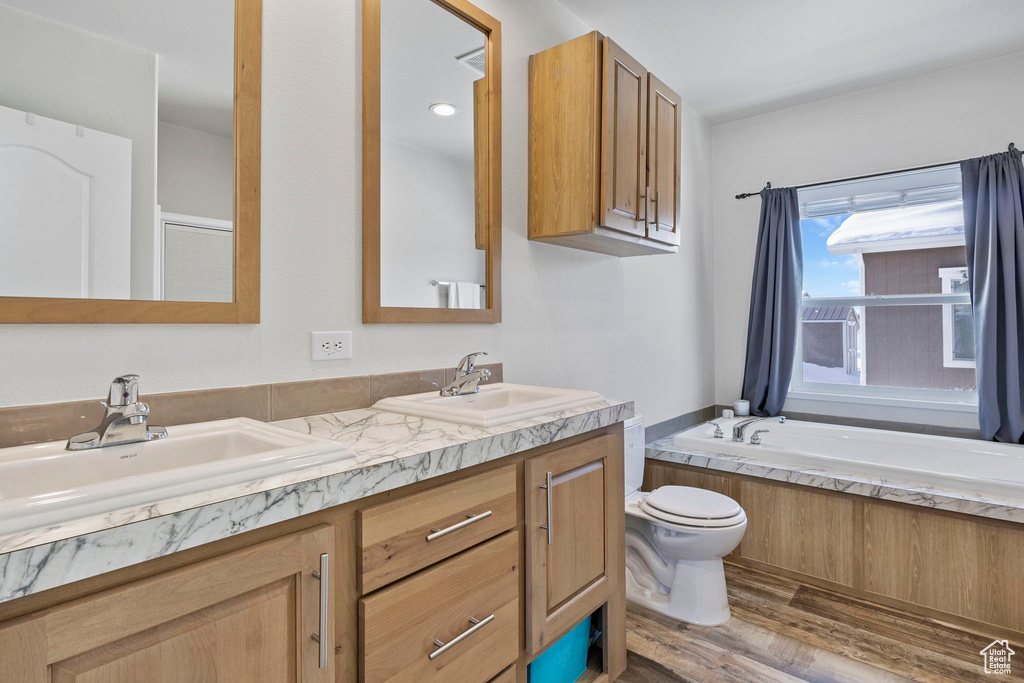 Bathroom with wood-type flooring, a bathtub, double sink vanity, and toilet