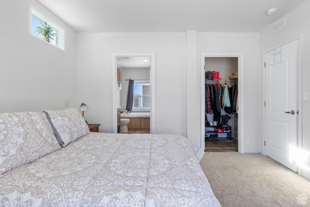Bedroom featuring a closet, ensuite bath, a walk in closet, and light colored carpet