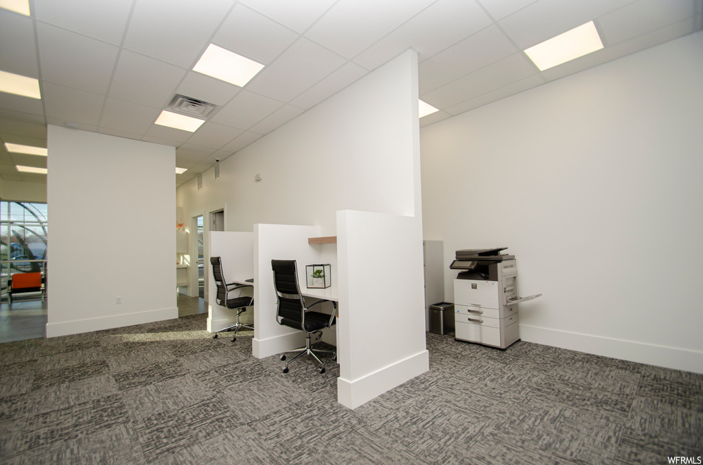 Office space with a towering ceiling, a drop ceiling, and dark carpet