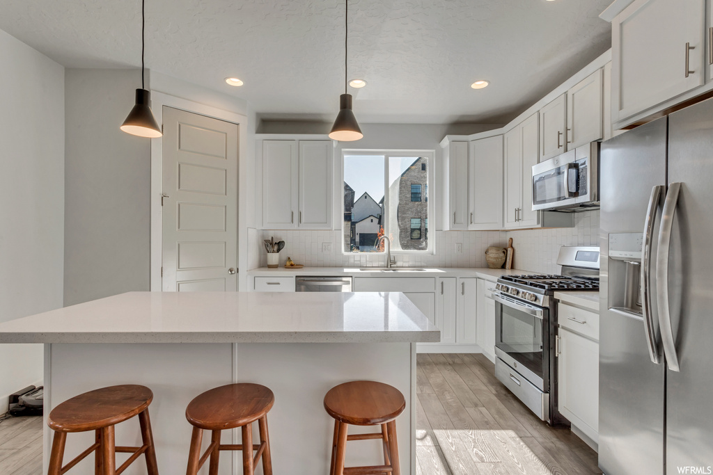 Kitchen featuring sink, hanging light fixtures, appliances with stainless steel finishes, white cabinets, and a kitchen island