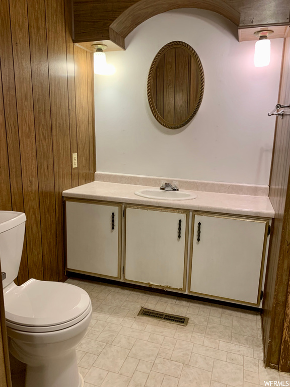 Bathroom with toilet, tile flooring, large vanity, and wooden walls