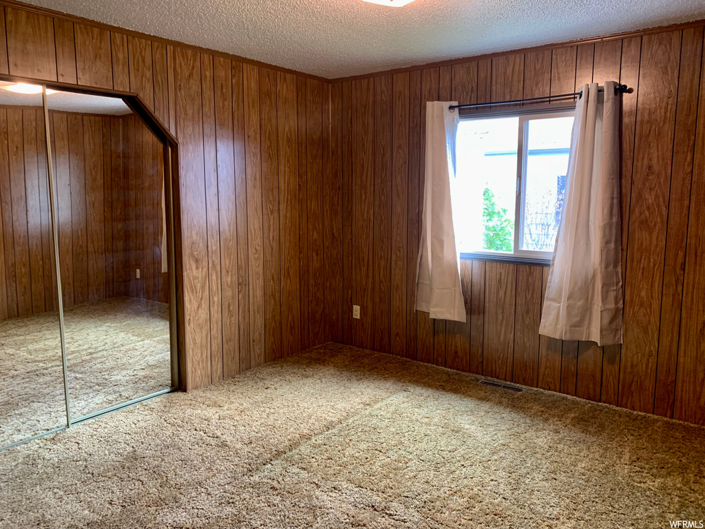 Unfurnished room featuring a textured ceiling, wooden walls, and carpet