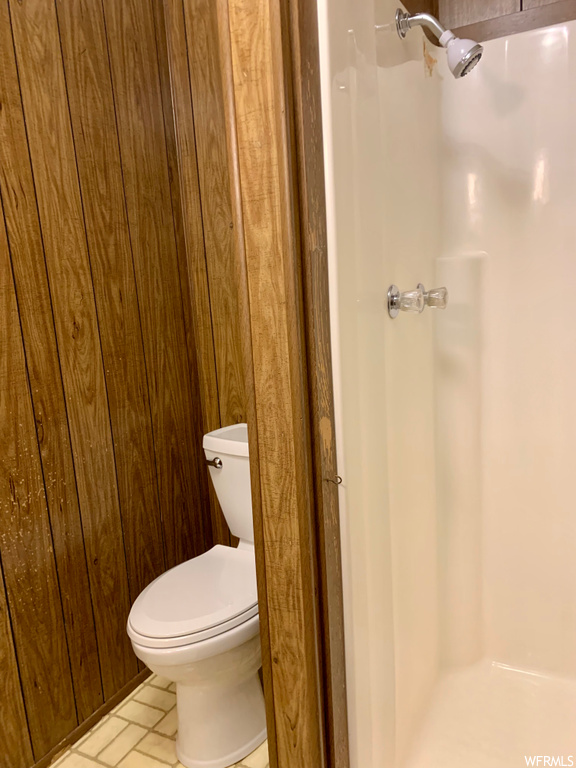 Bathroom featuring a shower, toilet, wood walls, and tile floors