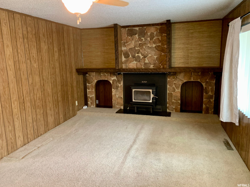 Unfurnished living room featuring wooden walls, light colored carpet, ceiling fan, and a fireplace