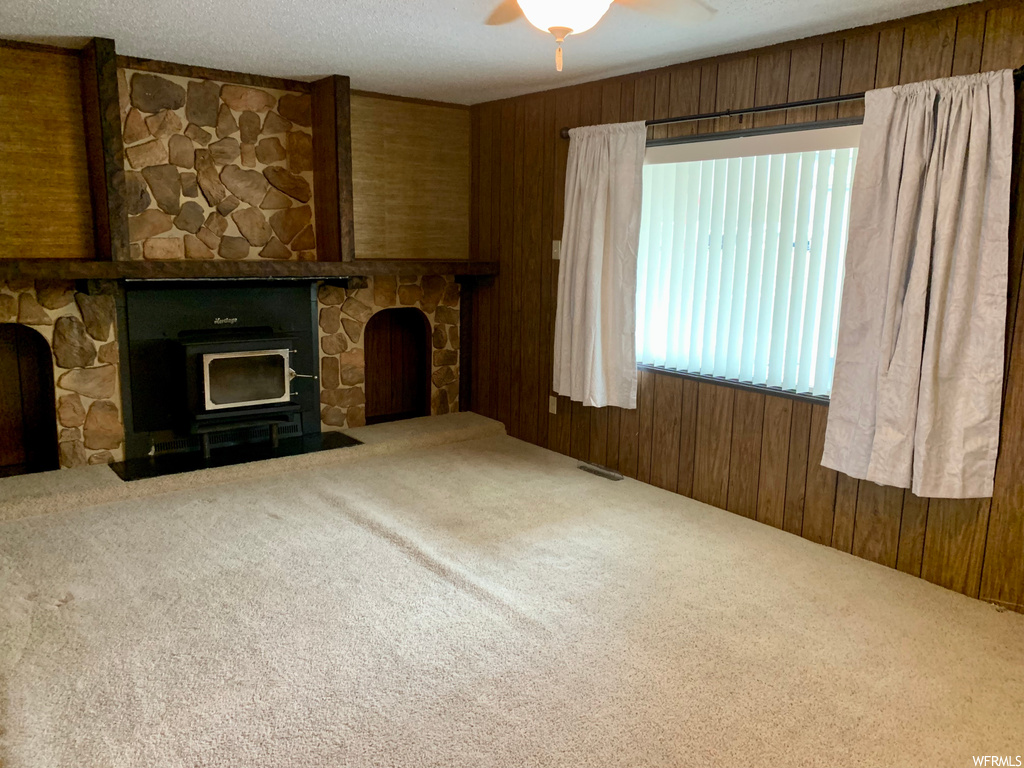Unfurnished living room featuring ceiling fan, a stone fireplace, carpet, and wooden walls