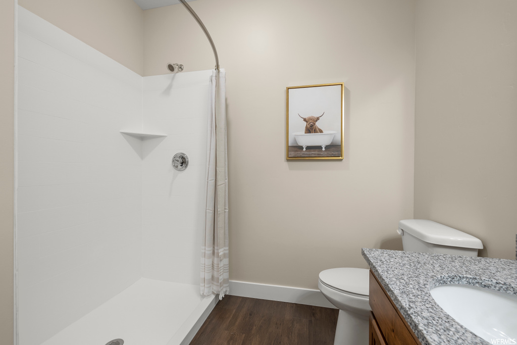Bathroom with toilet, vanity, a shower, and hardwood / wood-style flooring