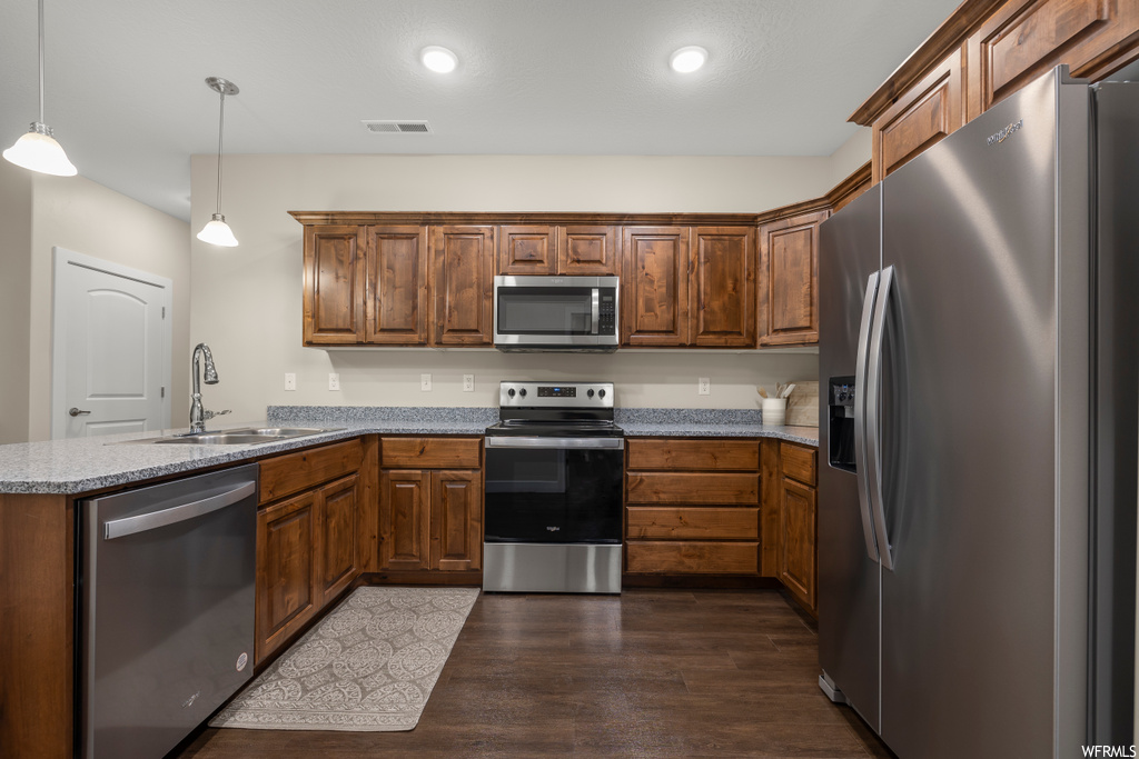 Kitchen with sink, stainless steel appliances, dark hardwood / wood-style flooring, decorative light fixtures, and kitchen peninsula