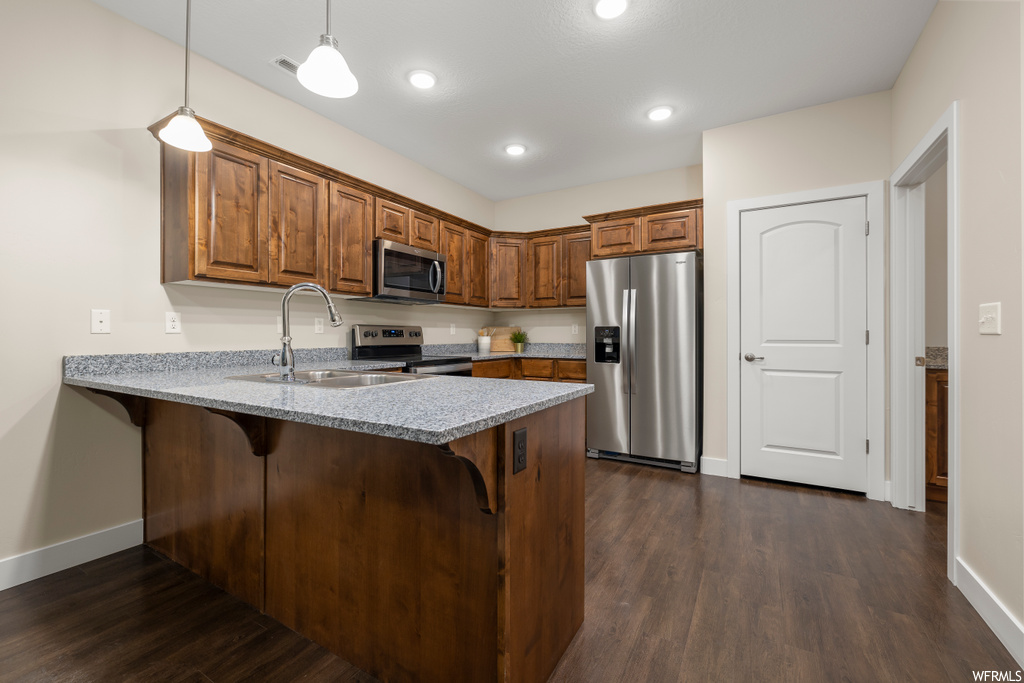 Kitchen featuring dark wood-type flooring, hanging light fixtures, sink, appliances with stainless steel finishes, and light stone countertops
