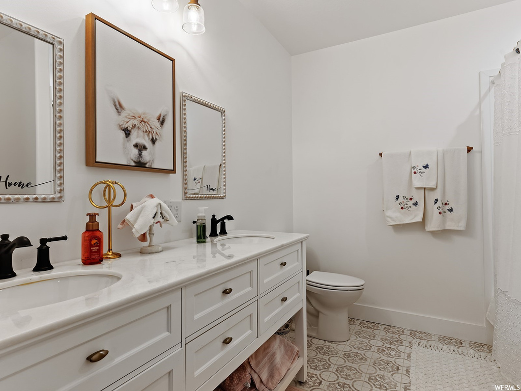 Bathroom featuring toilet, double sink, vanity with extensive cabinet space, and tile flooring