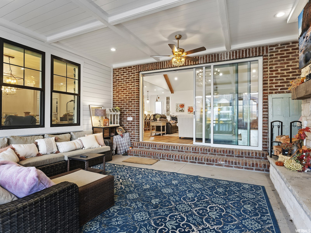 Living room featuring ceiling fan, light wood-type flooring, brick wall, and vaulted ceiling with beams