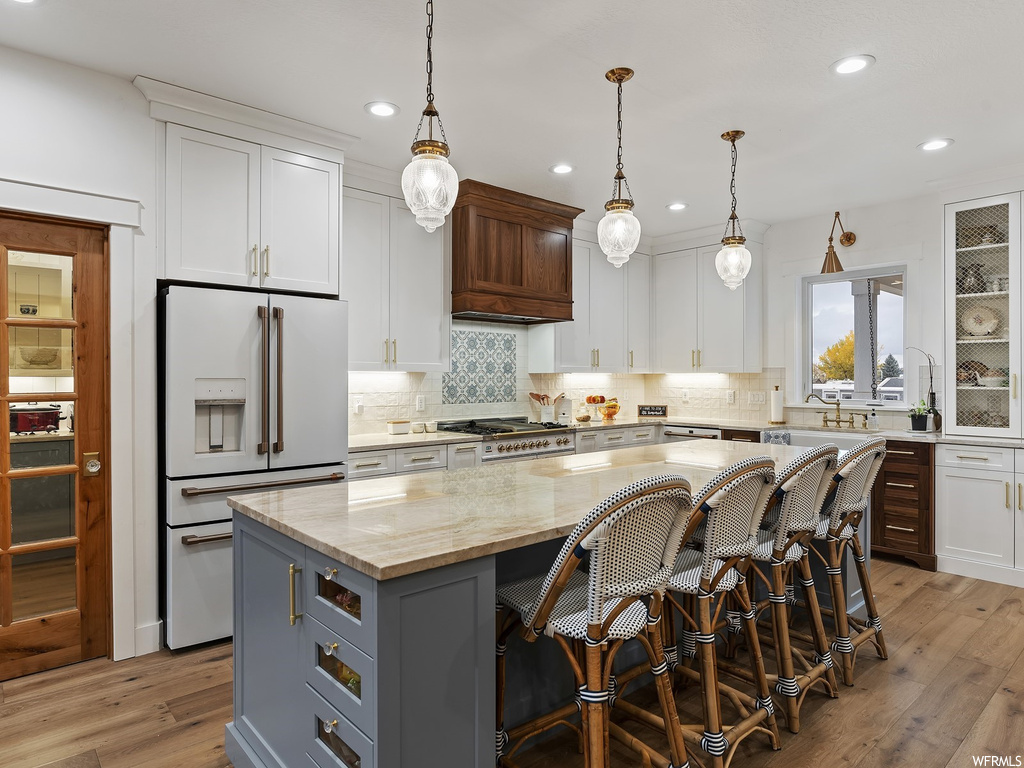 Kitchen with premium range hood, light hardwood / wood-style floors, a center island, high end white refrigerator, and white cabinets