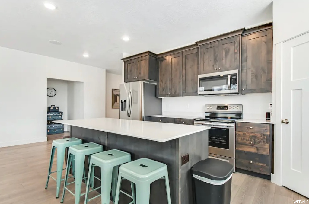Kitchen with a center island, dark brown cabinets, light hardwood / wood-style floors, stainless steel appliances, and a breakfast bar