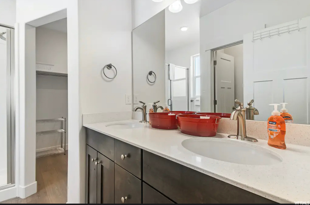 Bathroom featuring dual sinks, a shower with shower door, large vanity, and hardwood / wood-style flooring