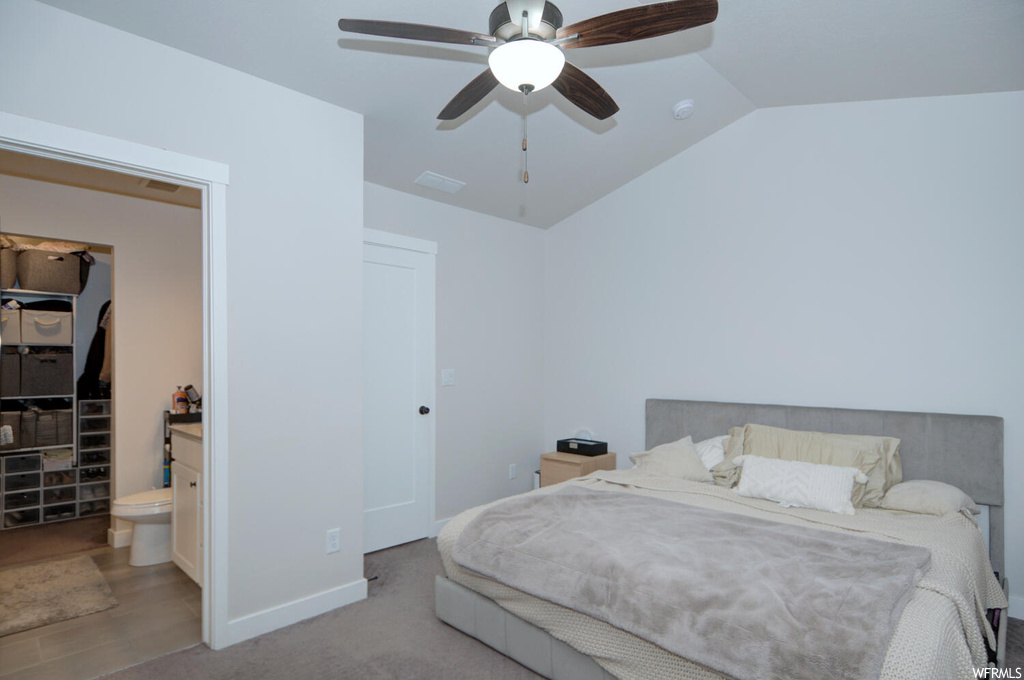 Carpeted bedroom featuring ensuite bathroom, ceiling fan, and vaulted ceiling