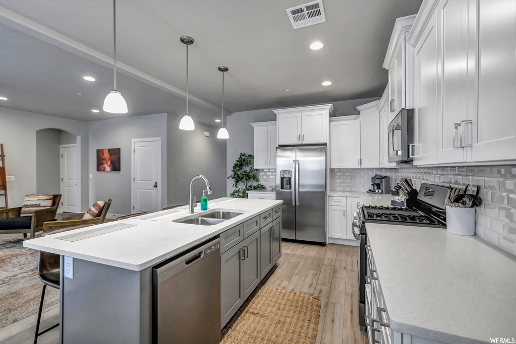 Kitchen featuring hanging light fixtures, a kitchen island with sink, stainless steel appliances, white cabinets, and backsplash