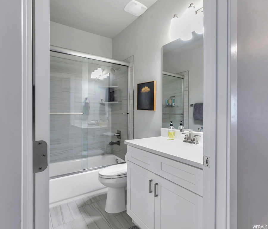 Full bathroom featuring toilet, combined bath / shower with glass door, tile floors, and vanity with extensive cabinet space